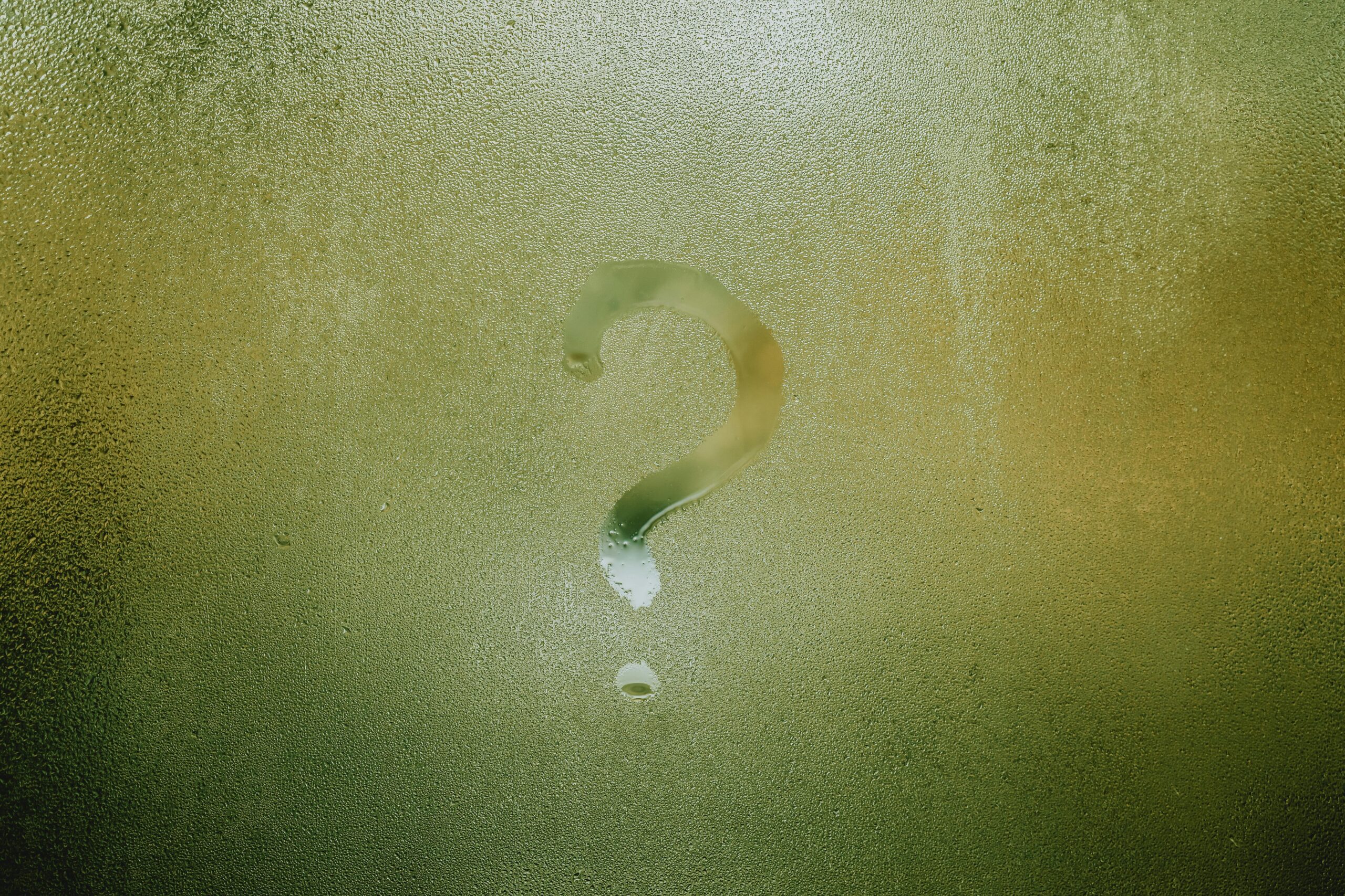 A question mark drawn on foggy glass, evoking curiosity and mystery.